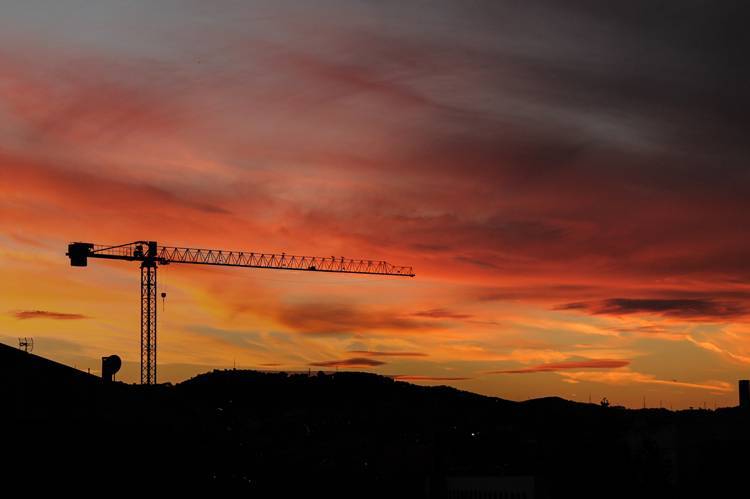 Construction site at sunset with buildings and cranes.
