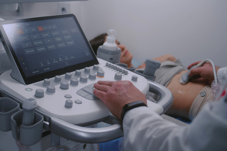 Close up of doctor using sonography machine with digital monitor. Medical specialist does ultrasound diagnostic to pregnant female patient. Modern clinic or medical center with advanced equipment. 