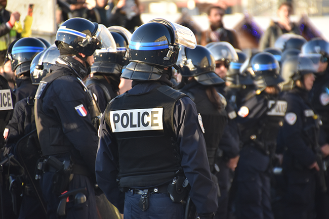 Line of police officers in riot gear with helmets and “POLICE” labels standing together at an outdoor event.