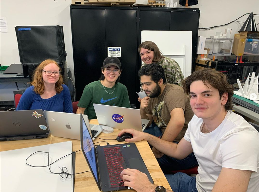 a small group shot shows students working around their computers smiling