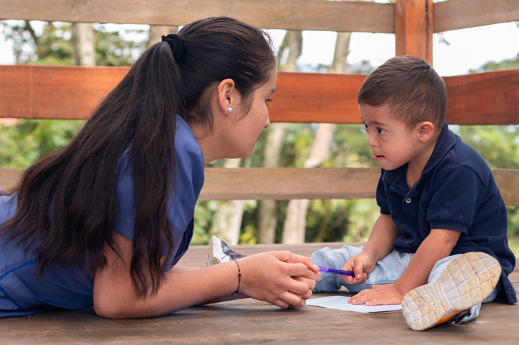 Woman in blue uniform teaching writing to a child with Down syndrome. Children's occupational therapy.