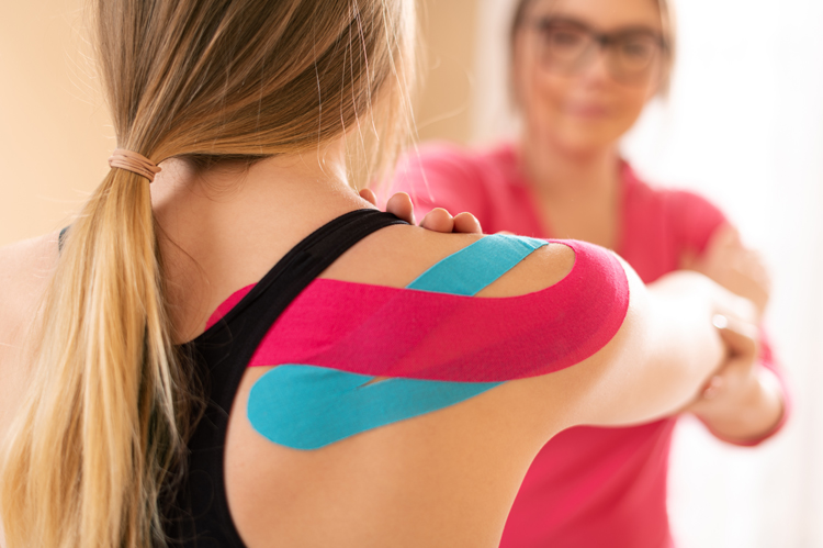 Young female patient wearing Kinesio tape on her shoulder exercising with a professional physical therapist. Kinesiology, physical therapy, rehabilitation concept.