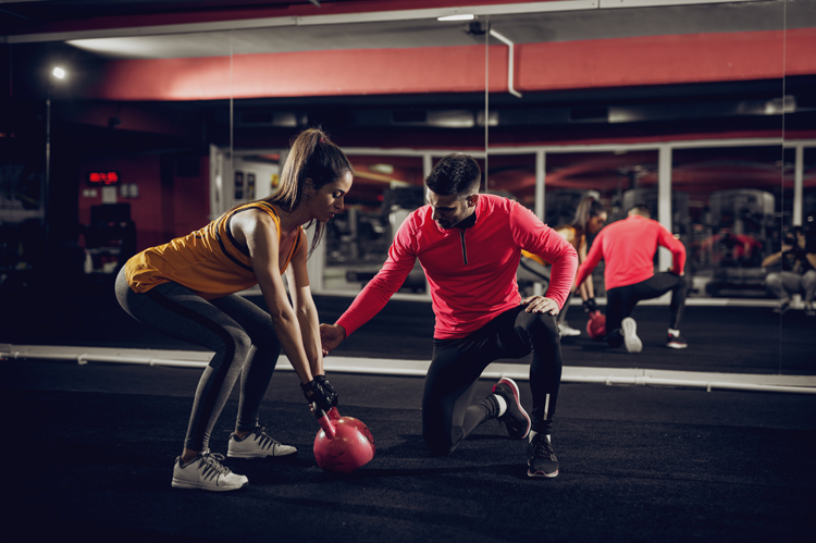 Young healthy focused sporty flexible shape girl with a ponytail doing squat exercises with the kettlebell.