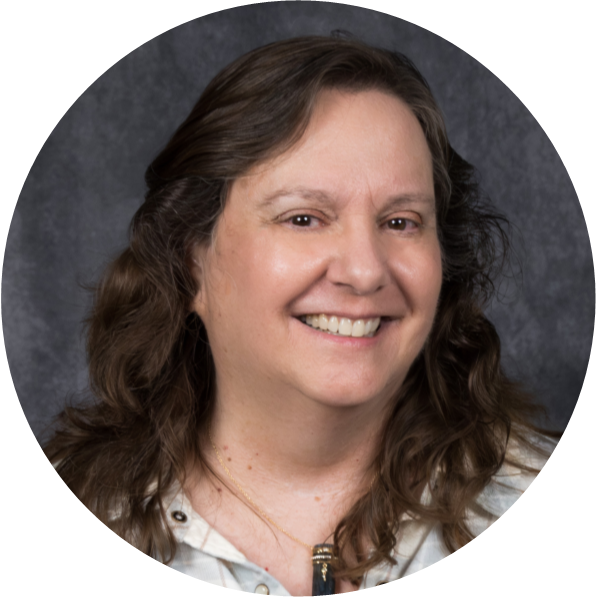 Professional headshot of a woman with long, wavy hair, smiling against a gray background.