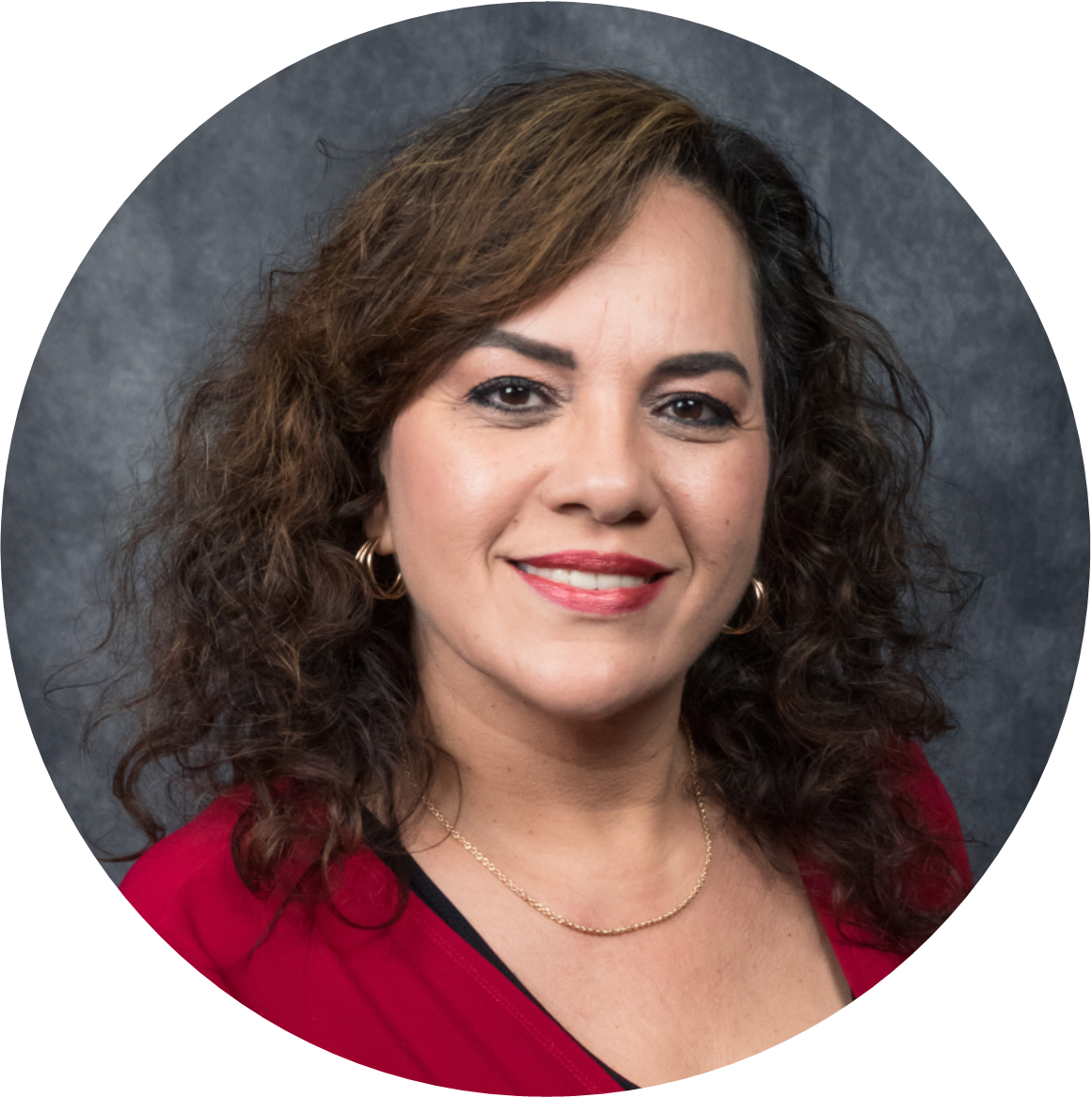 Professional headshot of a woman with curly hair wearing a red blouse, smiling against a gray background.