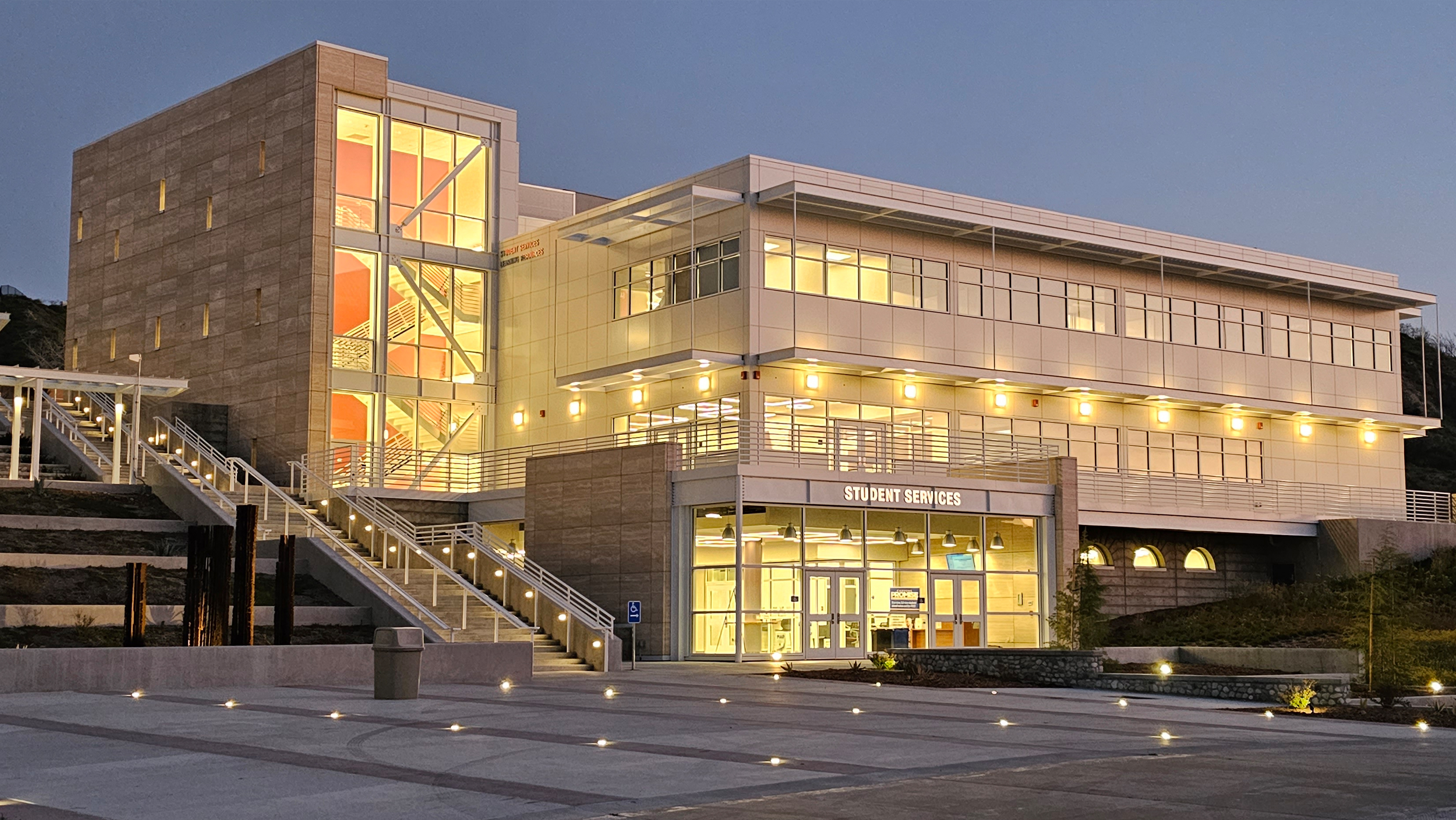 Modern student services building illuminated at dusk, featuring large windows and a contemporary design.