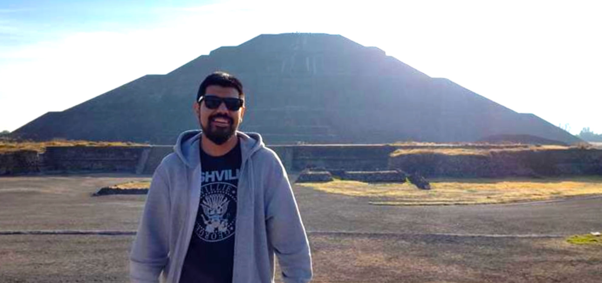 An image of man standing in front of an ancient pyramid.