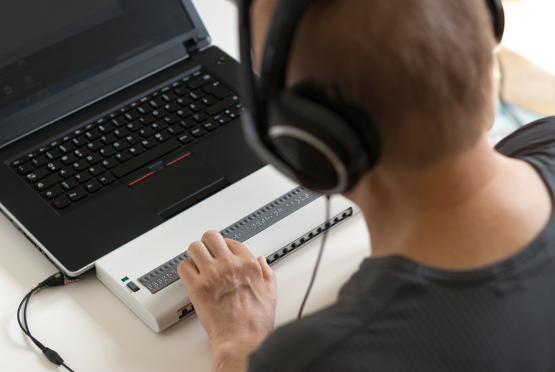 Blind person working on a computer with braille display and screen.