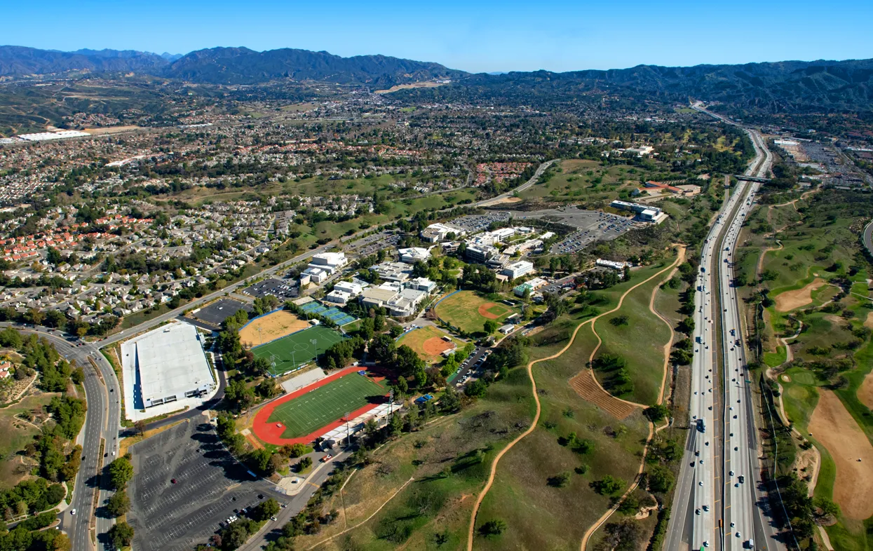 Aerial view of the Valencia campus with sports fields and a running track beside a highway, with hills and mountains in the distance.