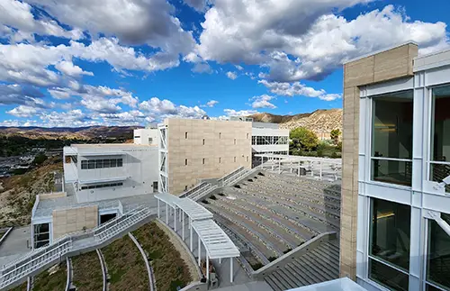 View of a modern architectural complex featuring an outdoor amphitheater and surrounding landscape under a cloudy sky.