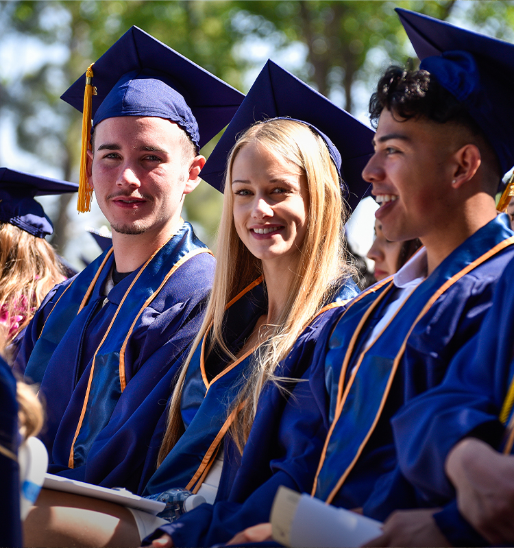 Students in caps and gowns smile during commencement.