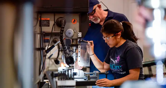 A female student operates machinery at the Advanced Technology Center under the watchful eye of an instructor..