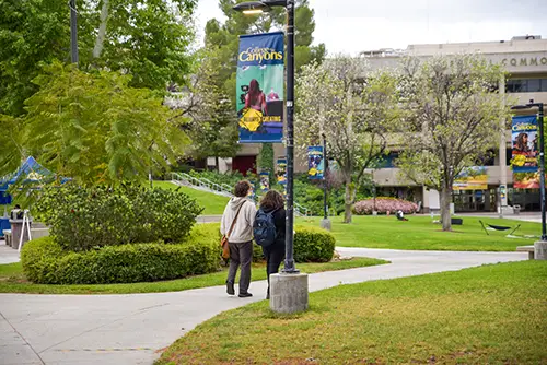 Two students walking on a Valencia campus pathway with banners displaying the college name.