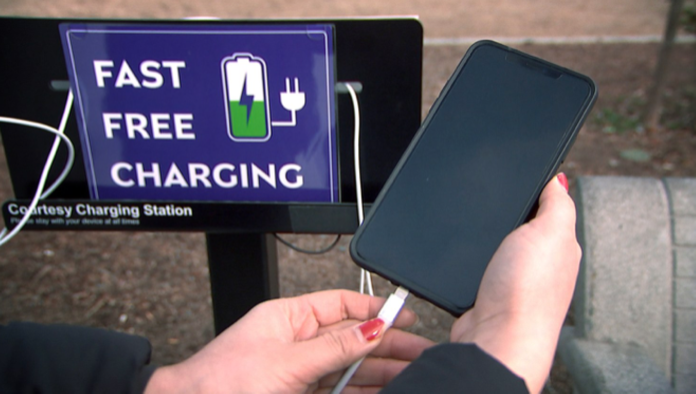a person holding a cell phone, plugging it into a public charging station