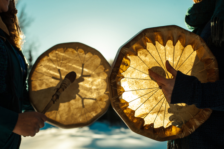 Women holding and playing their sacred drums outdoors in the wintertime.