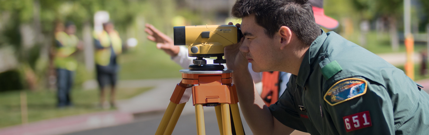 Boy Scout looking through surveying equipment.